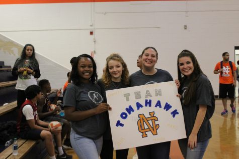 Excited fans Ashley Davis, Jules Shelly, Caroline Long, and Kallie Dever smile with posters to represent their team, Team Tomahawk. 