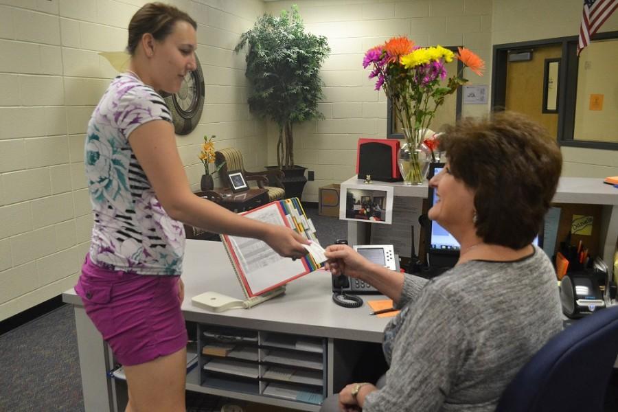 2015 classified employee of the year, Mary Stoll, hands senior mentor Danielle Mclarty a pass for a student. “I am honored to be the classified employee. Its an honor to be selected. I feel it is my role to help any of the NCHS staff with their needs. It feels great to have that effort validated,” said Stoll. 
