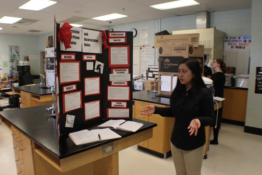 Kiky Etika shows off the data on her poster board to fellow junior Nathaniel Bigelow during the Posters Symposium.