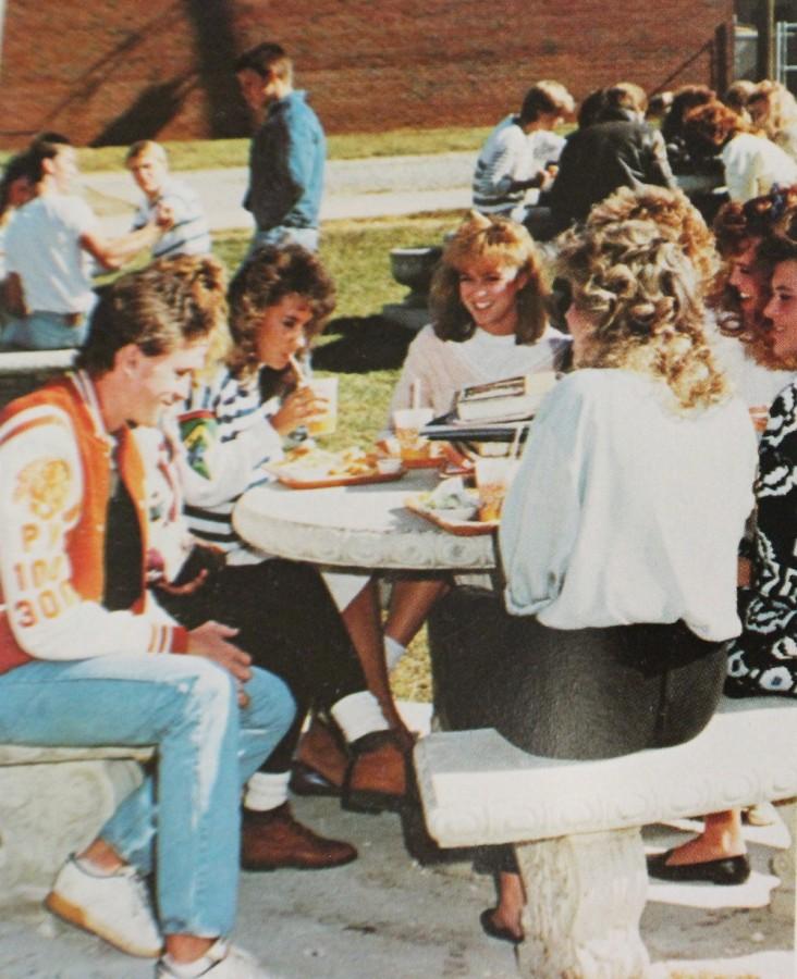 A 1988 NC yearbook shows a group of 8 friends enjoying the sunshine and eating lunch on the outside tables.