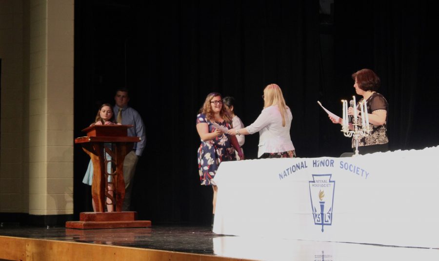 Junior+Jessica+Campbell+receives+her+certificate+and+identification+at+the+NHS+Induction+while+junior+Rebecca+Cantrell+signs+her+name+in+the+NHS+Induction+book%2C+awaiting+her+turn.