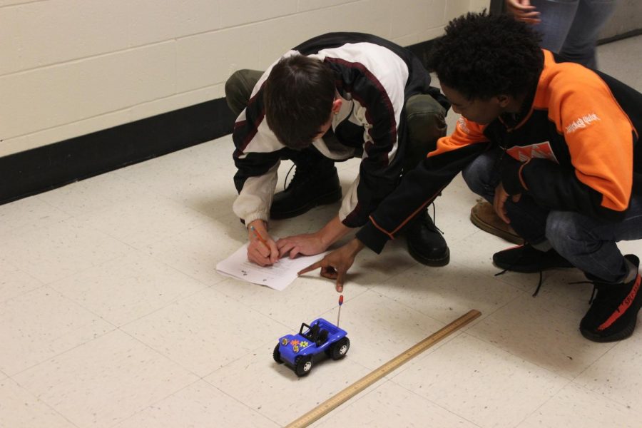 Mrs. Brennas third period class learns to graph the location of objects with constant velocity cars. The students paired into groups with rulers and toy cars to practice in the hallway.
