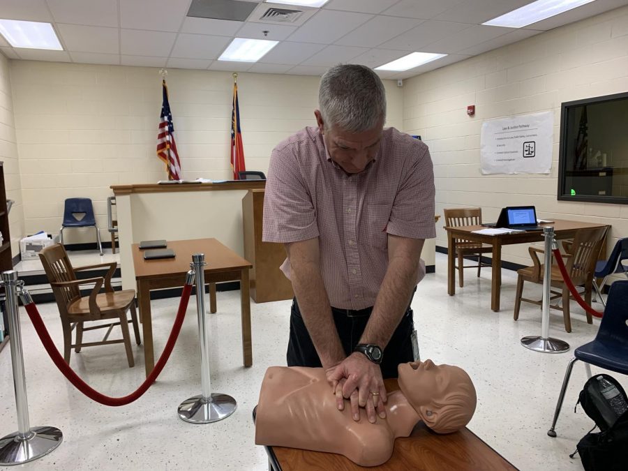 Dr. John Reagan demonstrates a typical CPR routine on a mannequin to show students how to properly perform CPR for his level two law class. “The most important thing is to recognize the emergency, and you want to make sure the scene is safe. Next, you want to check the victim to see if they are okay. Make sure you assist them [the victim] as quickly as you can to see what is going on, have one person call 911 while another person finds an AED. Then, look at the victim to make sure they are breathing.  If they are not breathing, you have to start CPR,” Reagan said. 
