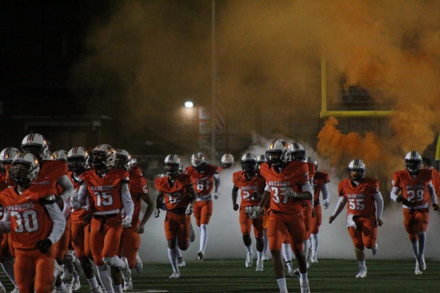 The+NC+varsity+football+team+runs+through+the+NC+banner+making+the+crowd+excited.+Orange+and+white+smoke+surround+the+players+as+they+jump+and+cheer+while+preparing+to+beat+North+Paulding.